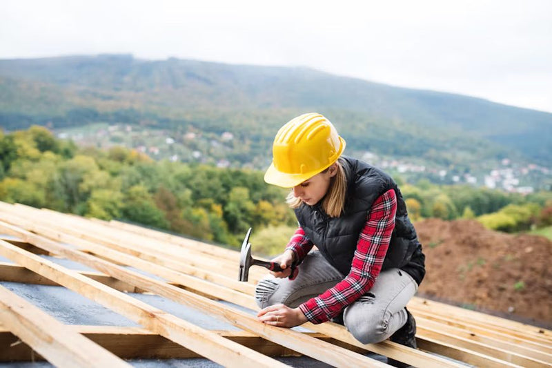 Roofer in a yellow hard hat hammering framing on a roof