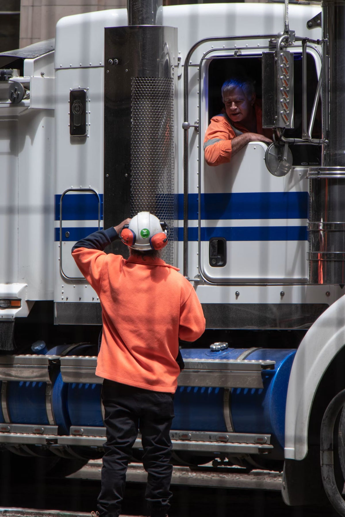 Worker in orange hi-vis and ear protection talking to a truck driver