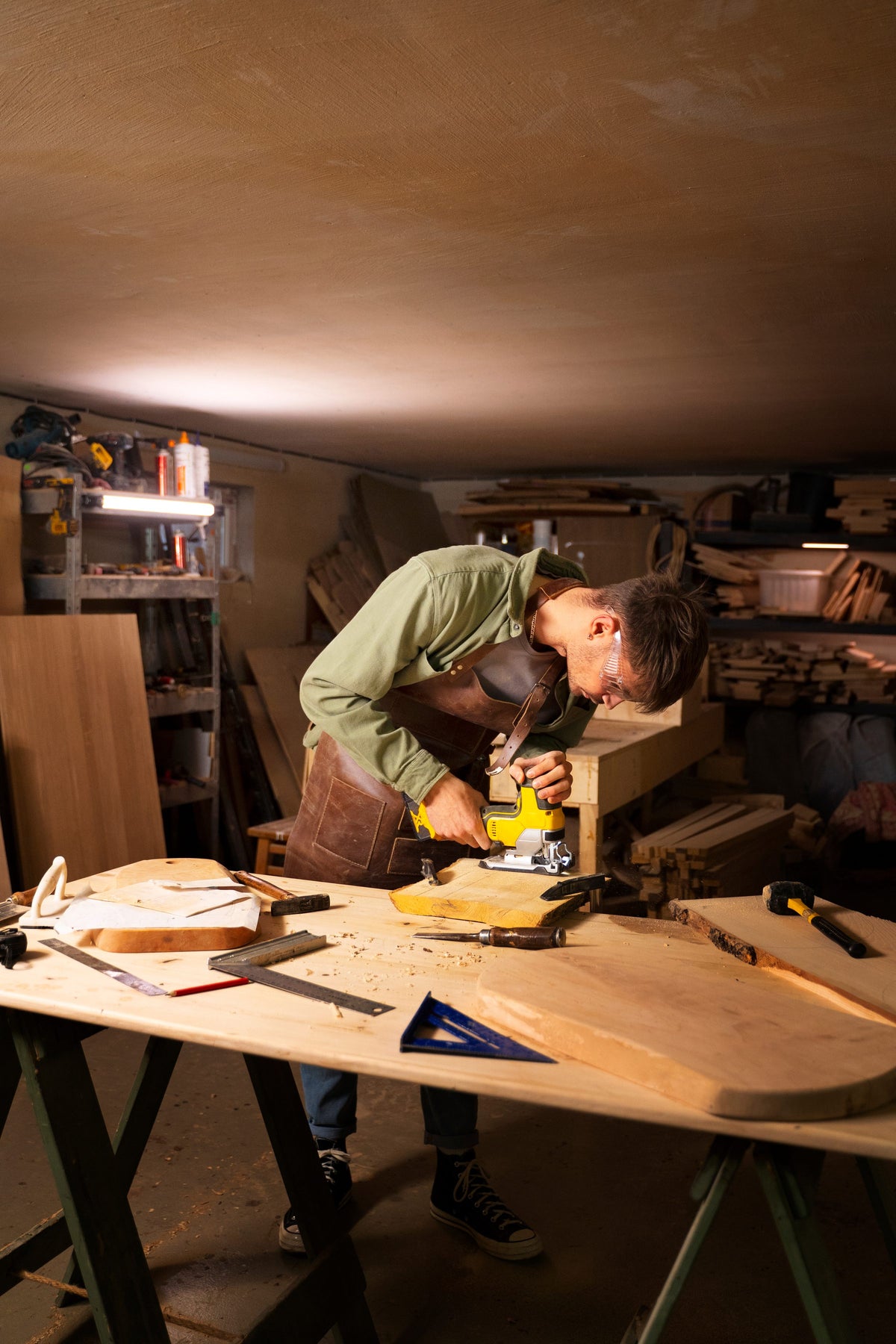 Carpenter cutting wood with a jigsaw in a dimly lit workshop