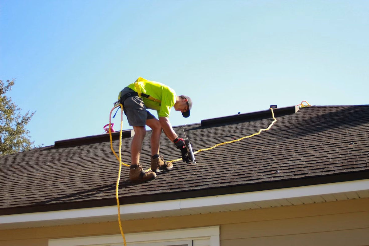Roofer in a hi-vis shirt working on a rooftop under a clear sky